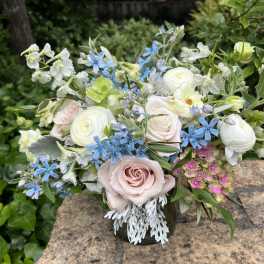 Mixed bouquet of pastel roses, white blooms, and blue flowers in a vase