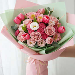 Pink bouquet with roses, tulips, and white blooms wrapped in pastel paper