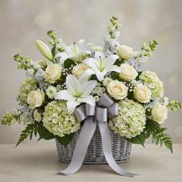White lilies and cream roses in a wicker basket with a silver ribbon