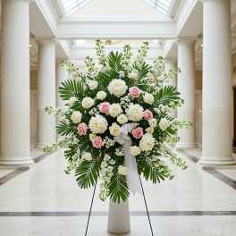 Large white and pink floral standing arrangement with palm leaves on an easel