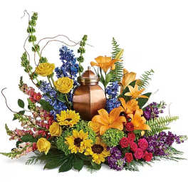 Colorful floral arrangement around a copper urn with yellow, orange, blue, pink, and purple blooms