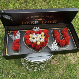Red roses arranged in a black gift box with gold accents and a "Happy Anniversary" topper