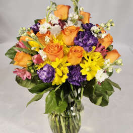 Mixed bouquet of orange roses, purple carnations, and yellow daisies in a glass vase