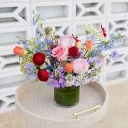 Mixed bouquet of roses, tulips, and blue flowers in a green glass vase