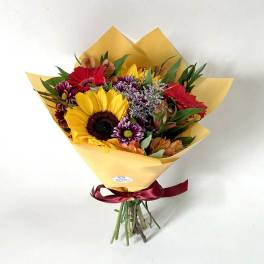 Mixed bouquet with a sunflower, red gerberas, and purple flowers in yellow wrap