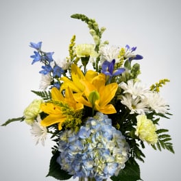 Bouquet of yellow lilies, blue hydrangea, and white daisies in a glass vase