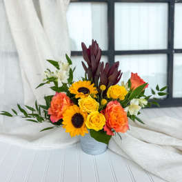 Mixed bouquet of yellow roses, sunflowers, and coral blooms in a metal container
