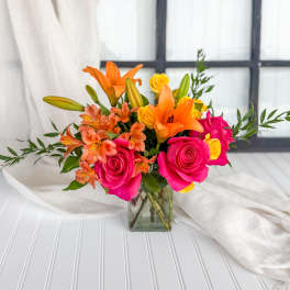 Bouquet of pink roses, orange lilies, and yellow blooms in a glass vase