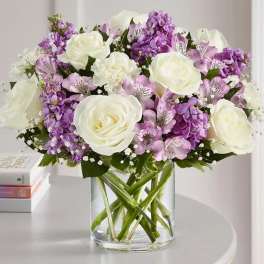 Bouquet of white roses and purple flowers in a clear glass vase