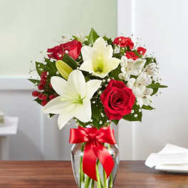 Bouquet of red roses and white lilies in a glass vase with a red ribbon