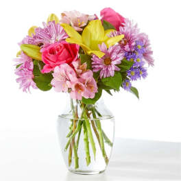Bouquet of pink roses, yellow lilies, and purple daisies in a glass vase