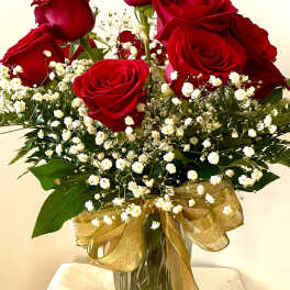 Red roses and baby's breath in a glass vase with a gold ribbon