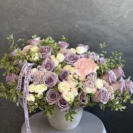 Lavender and cream roses arranged in a gray vase with greenery.