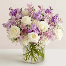 White roses and lavender flowers arranged in a clear glass vase