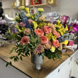 Mixed bouquet in a ribbed silver vase with pink, yellow, and blue flowers