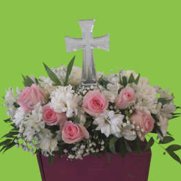 Pink roses and white flowers arranged around a clear cross in a purple container