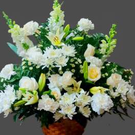 White floral arrangement in a woven basket with lilies and roses