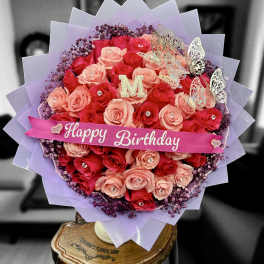 Round bouquet of red and peach roses with birthday ribbon and butterflies wrapped in lavender paper