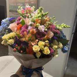 Mixed bouquet of colorful flowers wrapped in paper with a blue ribbon