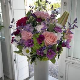 Mixed bouquet of pink, purple, and white flowers in a tall white vase