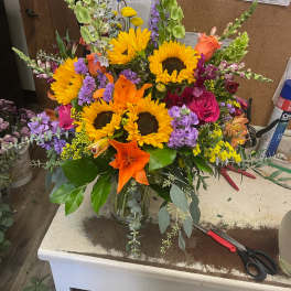 Bright mixed bouquet with sunflowers, lilies, roses, and purple spikes in a glass vase