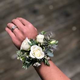 White rose wrist corsage with small white filler flowers worn on a wrist.