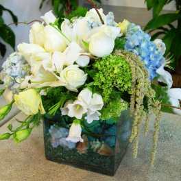 White and blue floral arrangement in a square glass vase