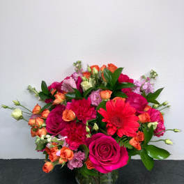 Mixed bouquet of pink, orange, and red flowers in a glass vase