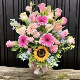 Tall mixed bouquet of pink roses and gerbera daisies with a sunflower in a glass vase