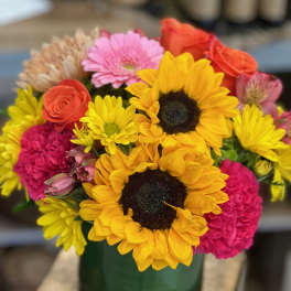 Bright mixed bouquet with sunflowers, roses, gerbera and carnations in a green glass vase
