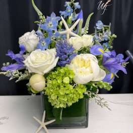 Blue and white floral arrangement in a square glass vase with starfish accents