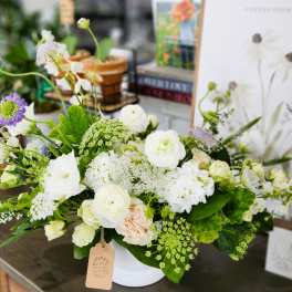 White and pale green floral arrangement in a white container
