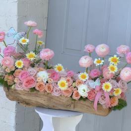 Pink and peach flower arrangement in a wooden container with daisies and butterflies