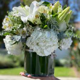 White floral arrangement in a glass vase with lilies and hydrangeas