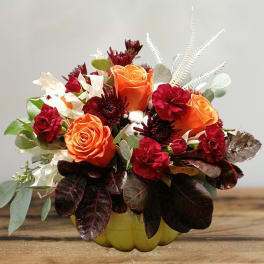 Orange and red rose arrangement in a yellow pumpkin container
