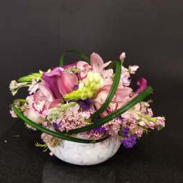 Pink and purple floral arrangement in a white bowl vase