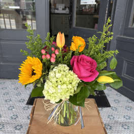 Mixed bouquet in a glass vase with a pink rose, sunflower, hydrangea, and tulips