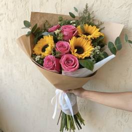 Bouquet of pink roses and yellow sunflowers wrapped in brown paper