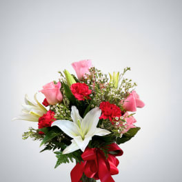 Bouquet of pink roses, white lilies, and red carnations in a glass vase with a red ribbon