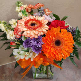 Mixed bouquet with orange gerberas and purple flowers in a glass vase
