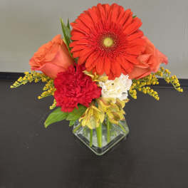 Bright mixed bouquet in a square glass vase with red and orange blooms