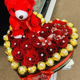 Heart-shaped bouquet of red roses with a red teddy bear and gold-wrapped chocolates