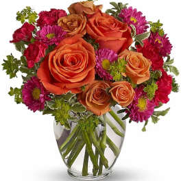 Orange roses and magenta daisies in a clear glass vase