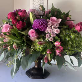 Large pink and purple floral arrangement in a dark pedestal vase