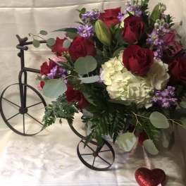 Bouquet of red roses, white hydrangea, and purple flowers in a decorative cart