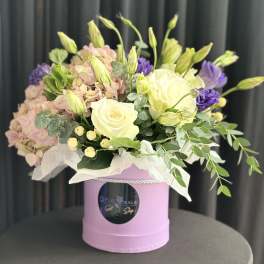 Bouquet of pale pink hydrangeas, white roses, and purple blooms in a pink box