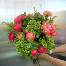 Handheld bouquet of pink and peach flowers with lush greenery