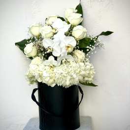 White roses and orchids in a black hatbox with hydrangeas