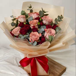 Bouquet of pink and red roses wrapped in beige paper with a red ribbon