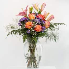 Mixed bouquet of pink lilies and orange roses in a glass vase